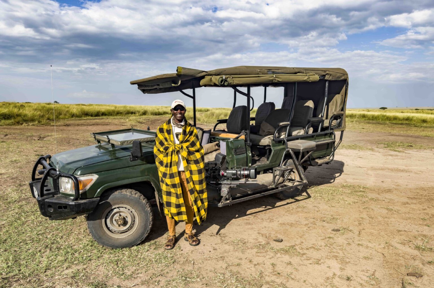 A Mlima photographic vehicle in the Maasai Mara with a cine camera on a side mount, and a Maasai driver-guide alongside